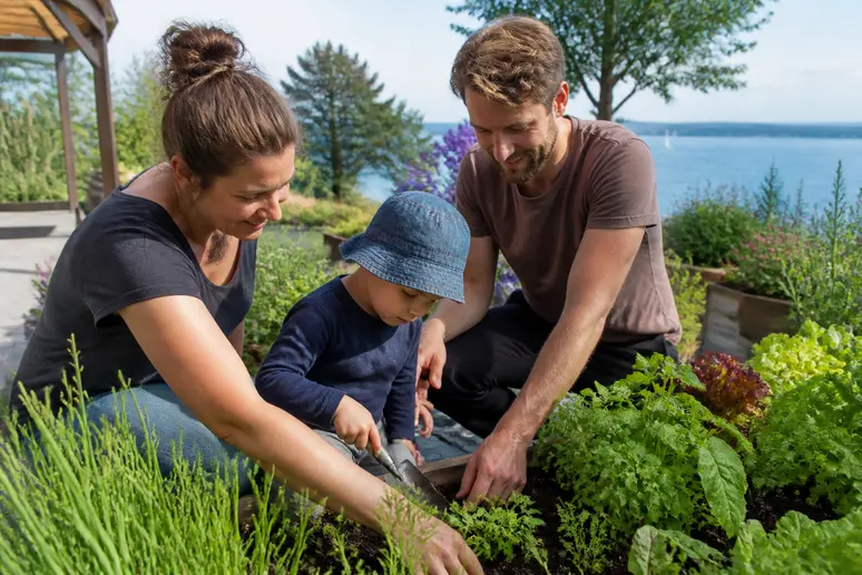 Familie im Garten am Bodensee: Eltern erklären dem Kind sichere Gartenarbeit mit Kirschlorbeer-Gefahren im Blick.