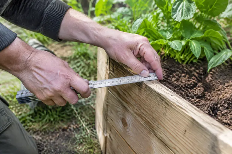 Messen der Beatlänge an einem Hochbeet im Garten als wichtiger Vorbereitungsschritt