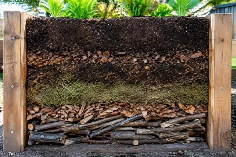 Querschnitt durch ein befülltes Hochbeet mit sichtbaren Schichten von Ästen bis zur Pflanzerde