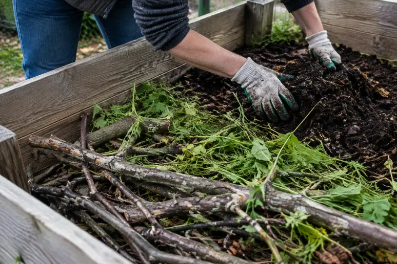 Schichtenaufbau mit grobem Schnittgut und Gartenabfällen beim Befüllen eines großen Hochbeets.